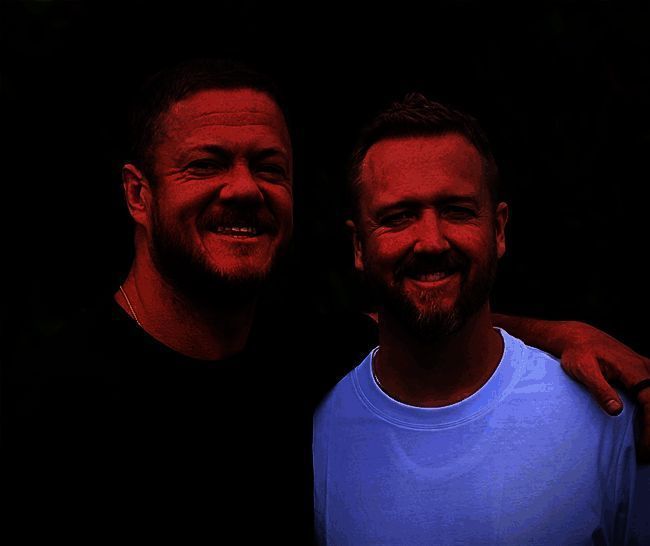 Night Street Games创始人Mac与Dan Reynolds兄弟合影，背景为游戏宣传海报