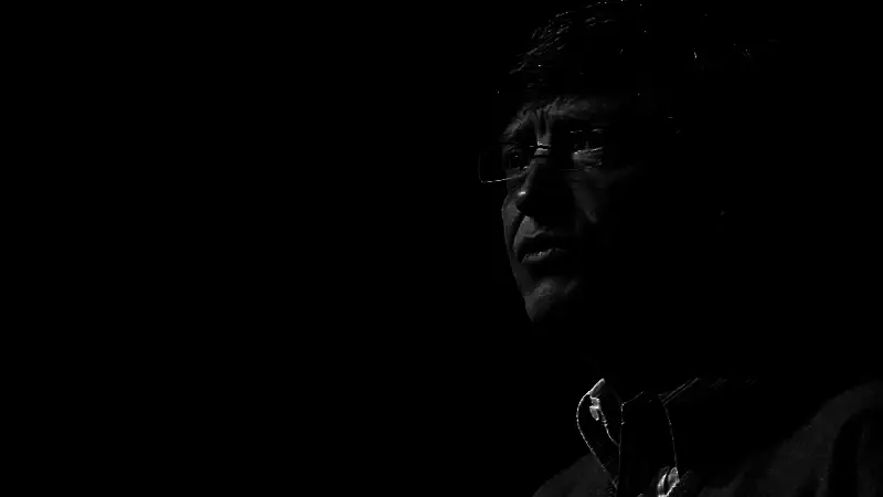 比尔·盖茨演讲画面，背景显示代码流与AI模型运行界面，突出人机协作主题