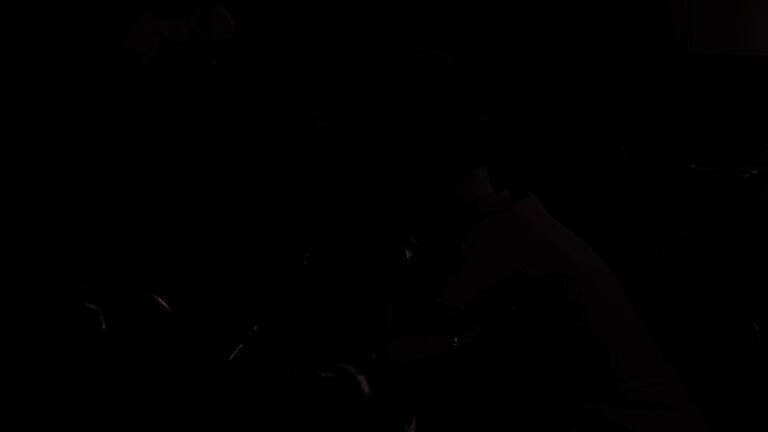 一位年长男性坐在沙发上专注操作手柄，屏幕显示《黑暗之魂》战斗画面，神情认真