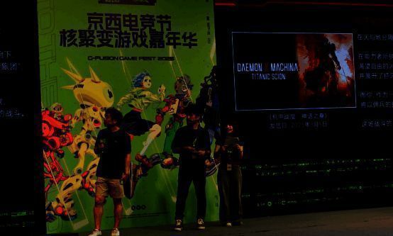 制作人佃健一郎在舞台上演示游戏画面，台下观众举机拍摄，反应热烈