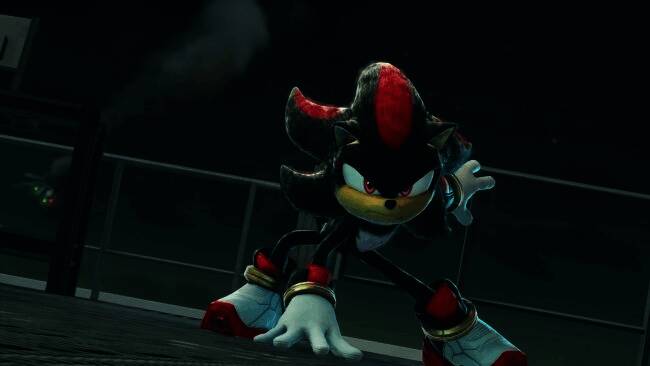 饭冢隆在采访中的照片，面带微笑坐在办公环境中，身后是索尼克系列的宣传海报