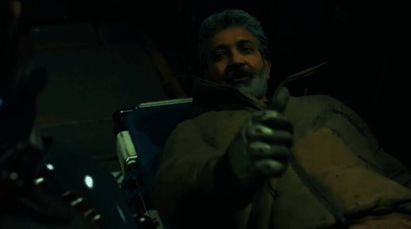 S.S.拉贾穆里与小岛秀夫握手合影，背景为印度风格艺术画作