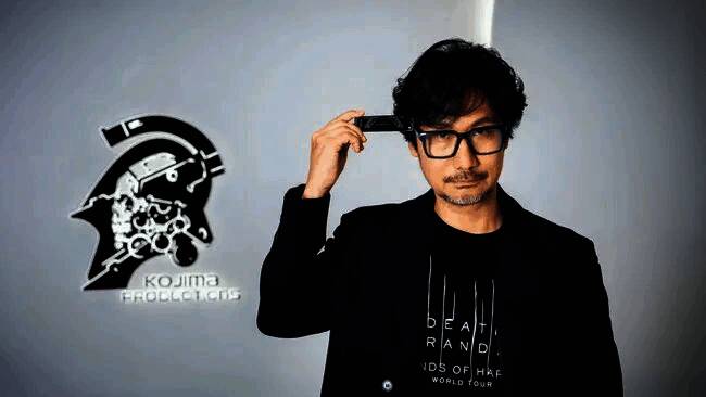 小岛秀夫在座谈会现场发言，神情专注，背景为大型会议屏幕展示其代表作画面