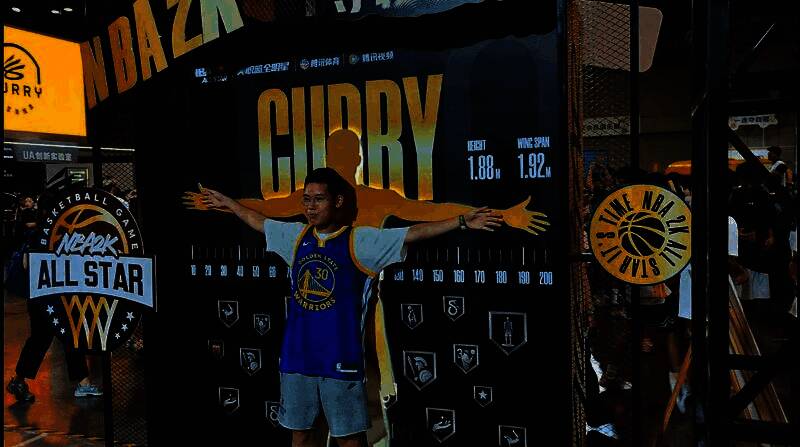玩家在NBA2K手游展区前与巨型海报合影，海报上是游戏内库里角色形象
