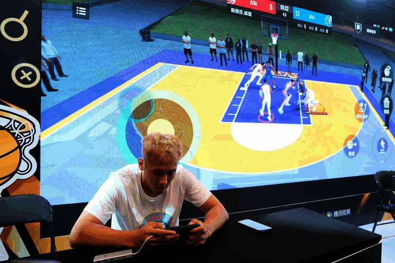 多位知名人士在NBA2K手游展台前合影，背景有游戏LOGO和库里元素