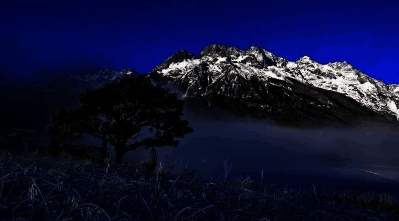 玉龙雪山实景摄影，雪峰耸立，云雾缭绕，山脚下绿意盎然，展现高原壮丽风光