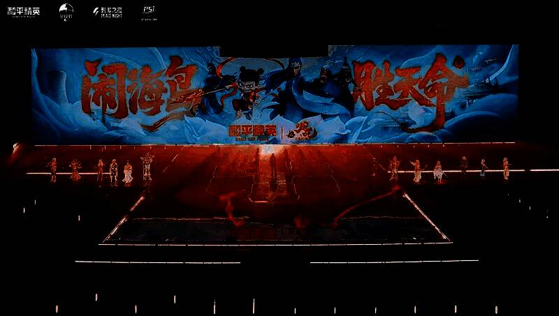 唐汉霄身穿红色国风电竞战衣，手持虚拟长枪，背后是哪吒三头六臂的巨幅投影