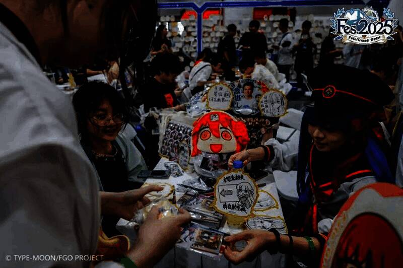 御主们在交流区围坐聊天，桌上摆放着角色徽章与周边，氛围温馨