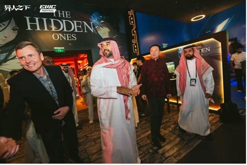 中国驻沙特大使与《异人之下》开发团队合影，背景为游戏宣传海报