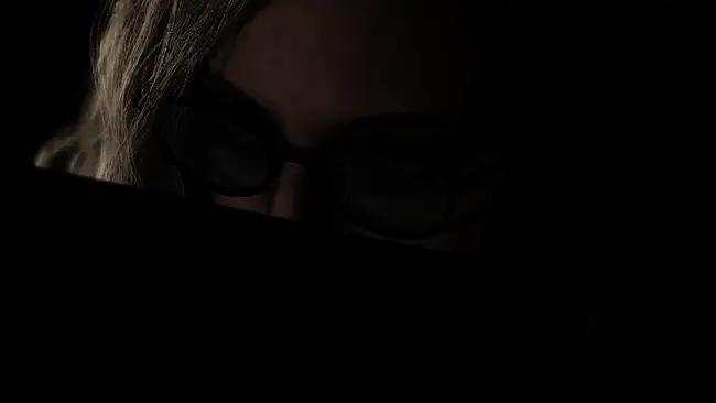 游戏中角色在昏暗实验室中转身面对未知威胁，背景可见破碎玻璃与血迹，气氛压抑