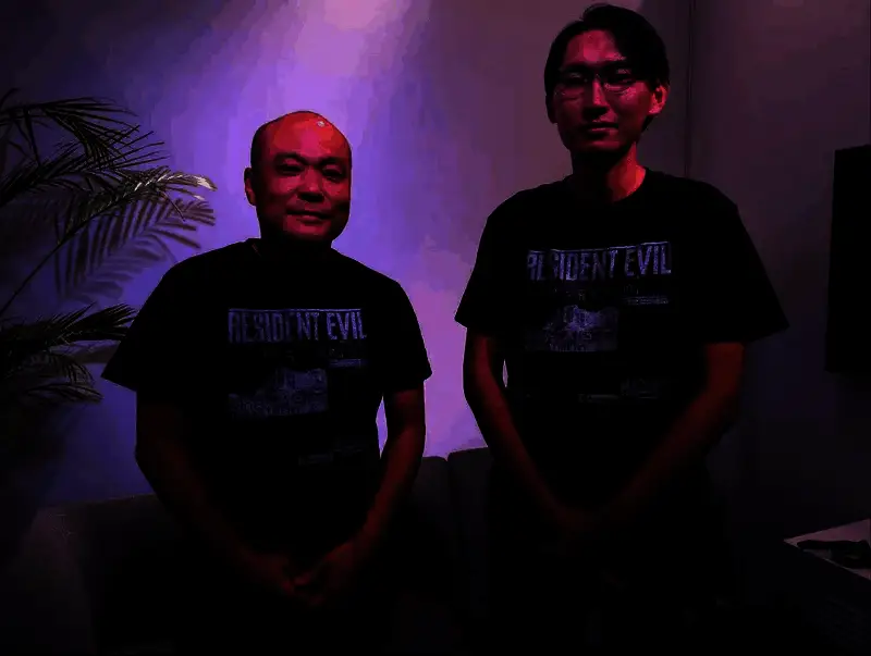 《生化危机9》开发团队合影概念图，众多工作人员围在标志性的病毒符号周围，气氛紧张而专业