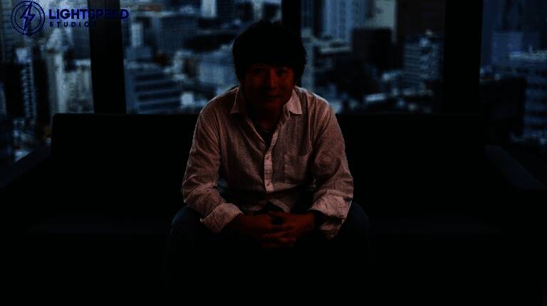 伊津野英昭在新工作室接受采访，背景为充满现代感的办公环境与游戏开发屏幕