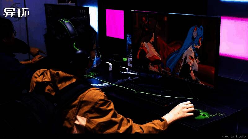 玩家正在试玩《异环》，屏幕上展示角色使用异能攀爬高楼的画面，周围工作人员协助引导