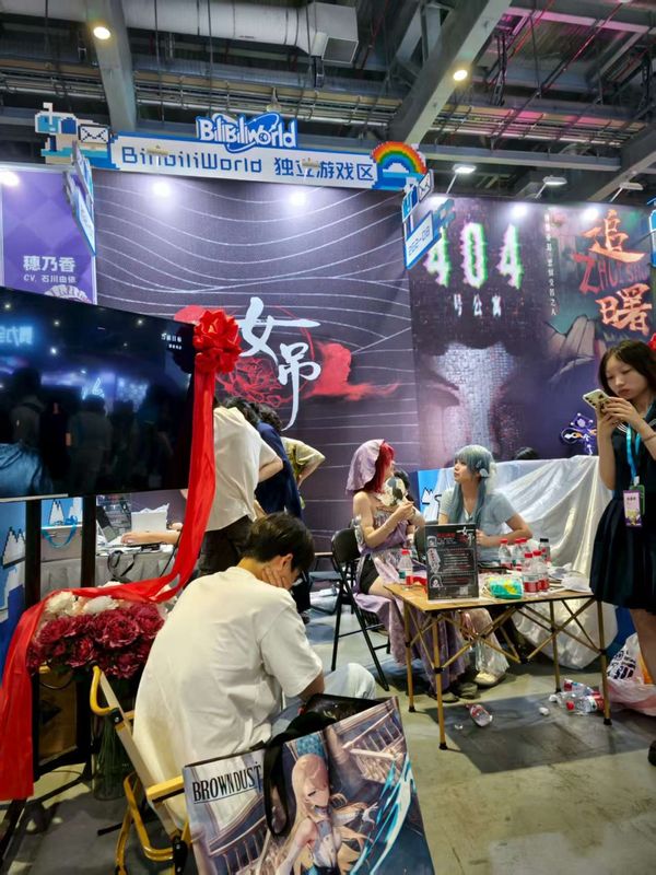 BW展会上玩家正在试玩《女吊》，屏幕显示昏暗祠堂场景，两人佩戴耳机神情专注