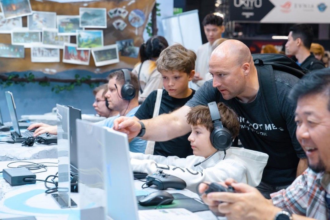 外国玩家专注试玩《山外山》，身后屏幕上显示角色正在搭建木屋，远处有巨兽出没