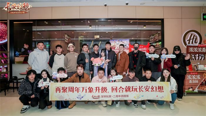 线下聚会现场照片，玩家们围坐火锅桌前欢笑合影，背景悬挂‘长安幻想二周年’横幅