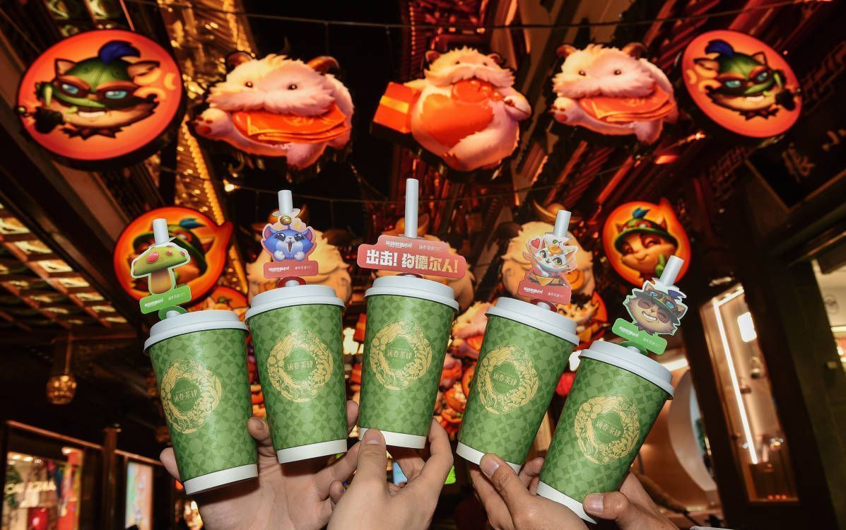 夜晚灯光璀璨的豫园街道，游客手持手机拍摄约德尔人花灯，背景是融合游戏风格的传统灯笼