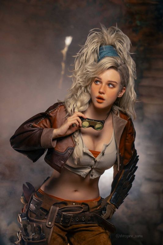 正面全身照，Sasha Holland 手持铁锤站立，身后是燃烧的熔炉与木质结构的铁匠铺