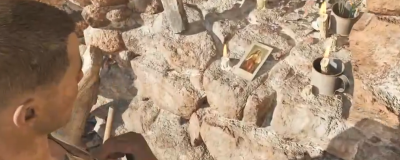 《四海兄弟：故乡》中一张圣徒卡片放置于古老石制神龛上的特写画面，周围布满蜡烛与鲜花，氛围庄重而神秘