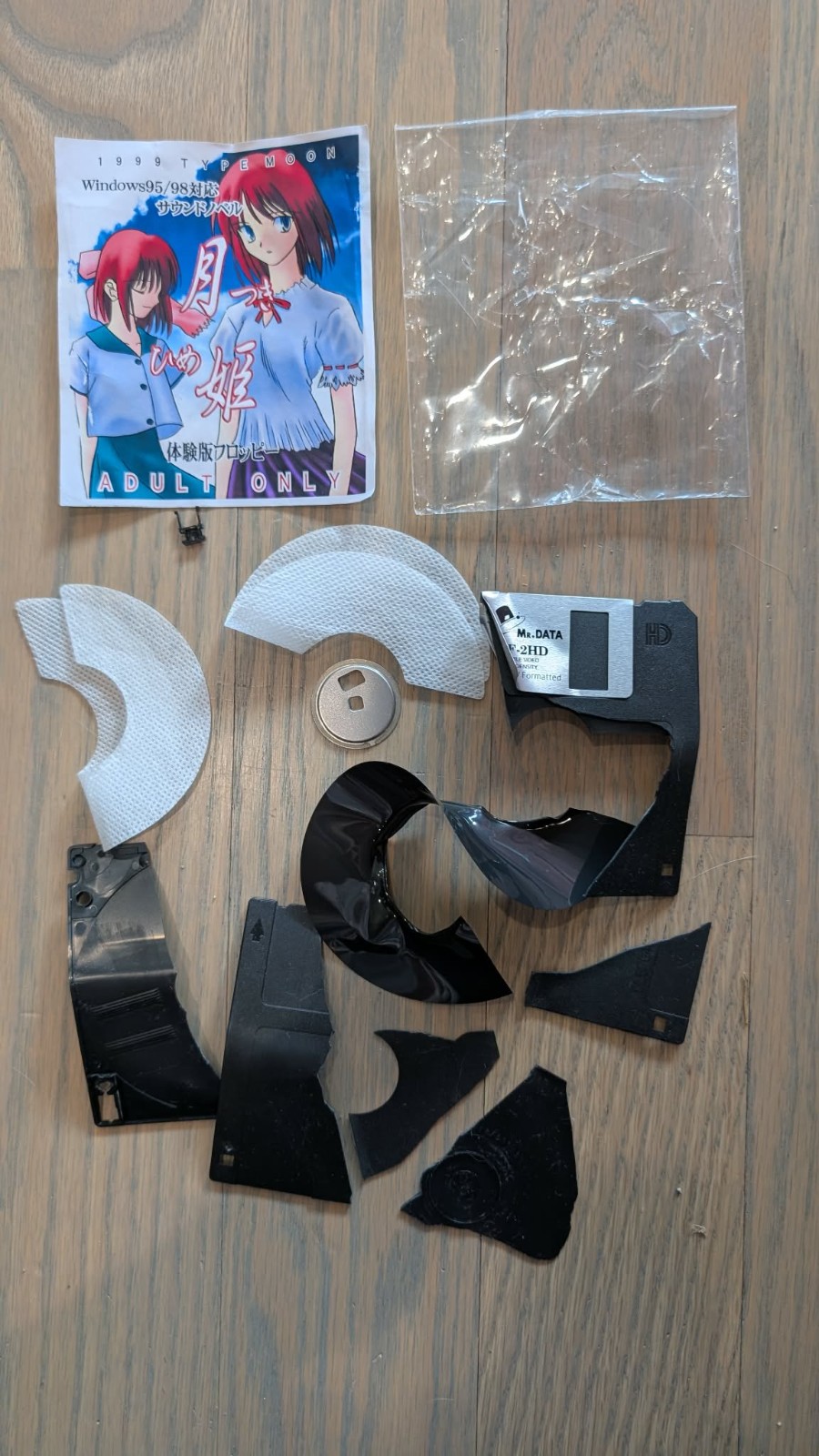 软盘包装细节图：透明塑料盒内衬薄层泡沫，盒盖手写编号‘#XX’，附带一张印有月姬角色剪影的迷你宣传卡