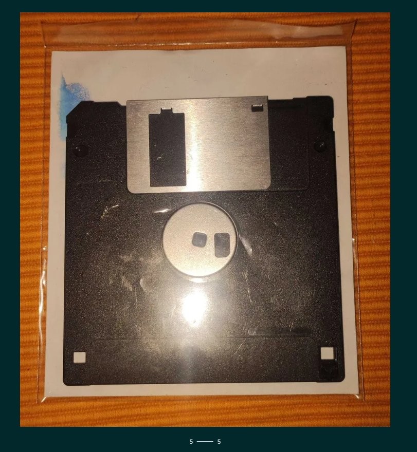 损毁后散落的软盘残片特写：数块不规则黑色塑料碎片，部分残留银色磁涂层，一枚金属滑盖扭曲变形