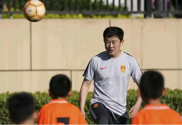 孙继海青训基地实景航拍图：现代化训练场与教学楼相邻而建，少年球员身着蓝白训练服进行分组对抗，教练手持平板实时记录数据